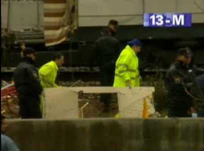 Unos operarios rodeados de policías pasan ante el coche 5 llevando una pieza que bien pudiera ser la que se ve arriba a la izquierda en la foto anterior