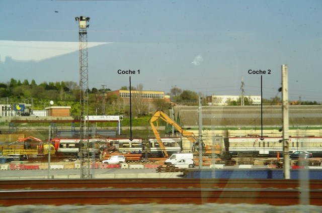 Tras atravesar el paso a nivel los tres coches de cabeza, se separa el coche 1 del 2. Hay máquinas trabajando, y un camión con grúa espera en el lado izquierdo. Detrás del coche 2, las naves industriales